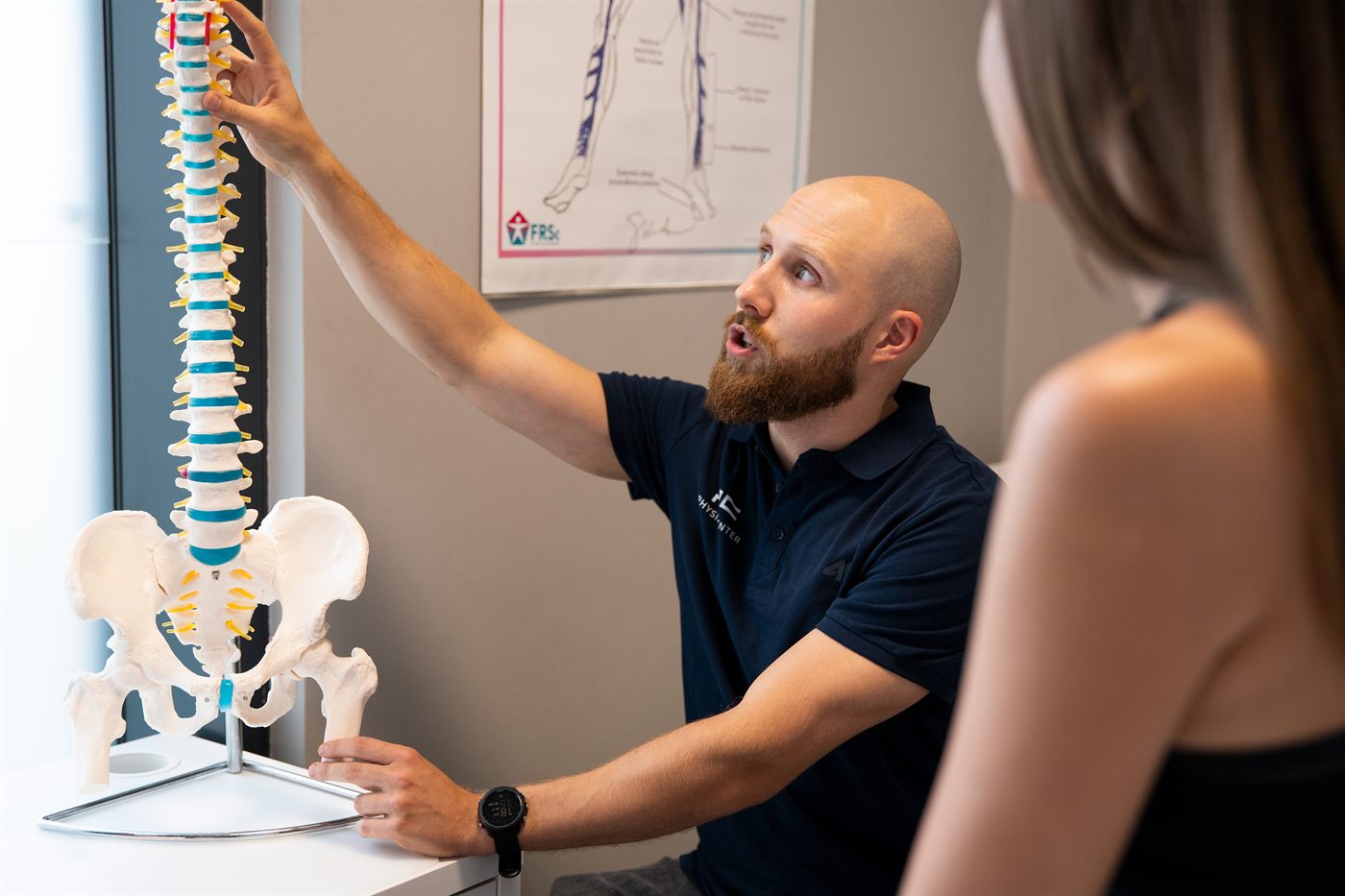 Fizjoterapeuta PhysioCenter tłumaczy pacjentce budowę kręgosłupa na modelu anatomicznym